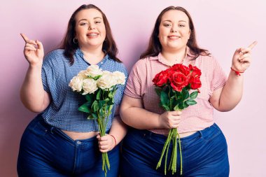 Çiçek tutan genç ve cüsseli ikizler mutlu bir şekilde elleri ve parmakları kenarda gezdiriyorlar. 