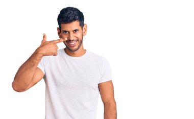 Gündelik kıyafetler giyen genç latin adam, el parmağı ve burnu işaret ederek, neşeyle gülümsüyor. güzellik konsepti 