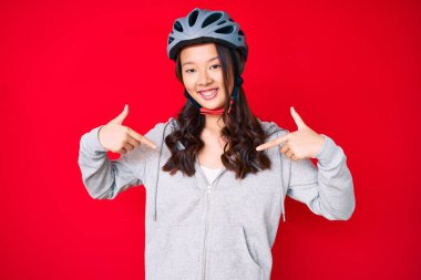 Bisiklet kaskı takan genç, güzel Çinli bir kız. Kendine güvenen, gülümseyen, kendini gururlu ve mutlu gösteren bir kız.. 