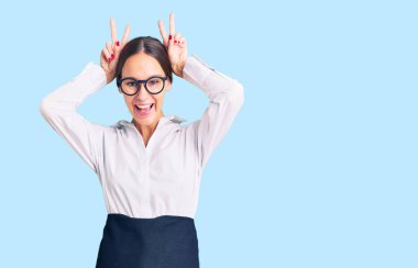 Güzel, esmer, profesyonel garson önlüğü giyen, komik ve çılgın pozlar veren, parmakları tavşan kulaklı, neşeli gülümseyen bir kadın. 