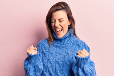 Kış süveteri giyen genç ve güzel bir kadın şaşkınlık ve şaşkınlık içinde kollarını kaldırarak ve gözlerini kapatarak başarıyı kutluyor. 