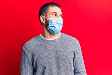 Tıbbi maske takan genç yakışıklı bir adam. Taraf arıyor, rahat poz veriyor, doğal bir yüz ve kendine güvenen bir gülümseme.. 