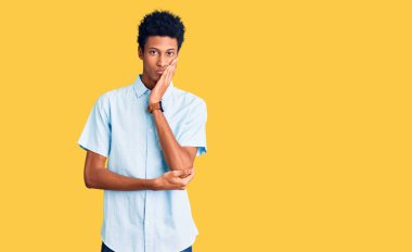 Genç, Afro-Amerikalı bir adam günlük kıyafetler giyip kollarını kavuşturup depresyondan sıkılmış ve yorgun görünüyor.. 