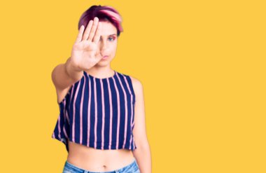 Pembe saçlı, günlük kıyafetler giyen genç ve güzel bir kadın avucunun içi gibi şarkı söylemeyi kesiyor. Yüzünde olumsuz ve ciddi bir jest olan uyarı ifadesi. 