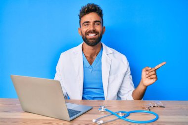 Klinikte çalışan İspanyol üniformalı genç adam gülümsüyor. Elleri ve parmakları kenarda mutlu bir şekilde işaret ediyor. 