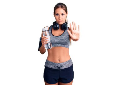 Genç ve güzel İspanyol kadın spor kıyafetleri içinde elinde su şişesiyle dur işareti yapıyor ciddi ve kendinden emin bir ifadeyle, savunma jesti yapıyor. 