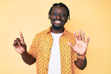 Saçları örgülü genç Afro-Amerikalı adam altı numarayı gösterip gösterirken kendinden emin ve mutlu gülümsüyor.. 