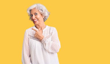 Son sınıf gri saçlı, günlük kıyafetler giyen, neşeli yüzlü, elleri ve parmaklarıyla gülümseyen mutlu ve doğal bir ifade takınan bir kadın. 