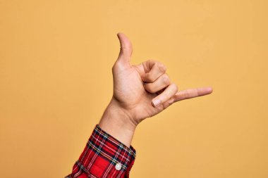 Kafkas genci parmaklarını izole edilmiş sarı arka planda gösteriyor Hawaii Shaka selamlama hareketi, telefon ve iletişim sembolü.