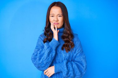 Genç, güzel Çinli bir kız diş ağrısı ya da diş hastalığından dolayı gündelik bir kazak giyip ağızlarına acı dolu bir ifadeyle dokunuyor. dişçi 