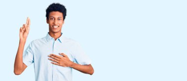 Genç, Afro-Amerikan bir adam günlük kıyafetler giymiş, gülümsüyor, elleri göğsünde ve parmakları havada küfür ediyor, sadakat yemini ediyor. 