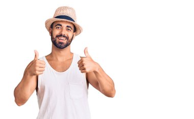 Gündelik yaz şapkası takan genç İspanyol adam elinle olumlu jest yapıyor, gülümsüyor ve mutlu. Neşeli ifade ve kazanan jest. 