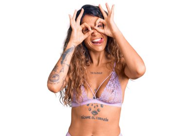 Dürbünlü dürbün gibi jest yapan, parmaklarından bakan, dövmeli genç İspanyol kadın. çılgın ifade. 