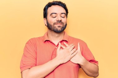 Gündelik kıyafetler giyen genç İspanyol adam elleri göğsünde gülümsüyor, gözleri kapalı ve yüzünde minnet ifadesi var. sağlık kavramı. 