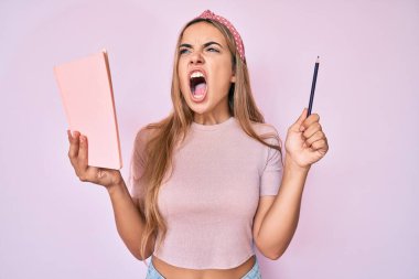 Genç, sarışın bir kadın elinde kitap ve kalem tutarken sinirli ve öfkeli çığlıklar atıyor öfkeyle bağırıyor. öfke ve agresif konsept. 