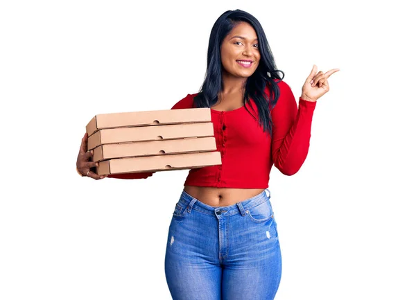 西班牙裔女人 留着长发 提着披萨盒 高兴地微笑着 手指手画脚地指向旁边 — 图库照片