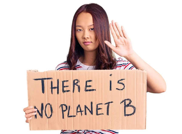 Young beautiful chinese girl holding there is no planet b banner with open hand doing stop sign with serious and confident expression, defense gesture