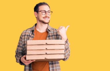 Elinde pizza kutusu olan yakışıklı beyaz bir adam başparmağını yana kaldırmış, ağzı açık gülümsüyor. 