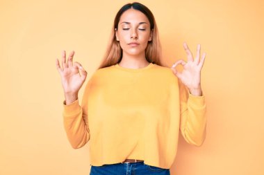 Sarı arka planda genç esmer kadın rahatla ve gözleri kapalı gülümse parmaklarıyla meditasyon hareketi yapıyor. yoga konsepti. 