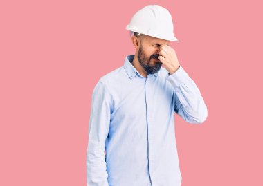 Mimar şapkası takan genç yakışıklı adam yorgun burnu ve gözleri ovuşturup yorgun ve baş ağrısı çekiyor. Stres ve hüsran kavramı. 