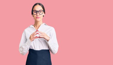 Profesyonel garson önlüğü giymiş güzel esmer bir kadın ellerini birleştirip gülümseyerek gevşemiş ve neşeli olmasını diliyordu. Başarı ve iyimserlik 