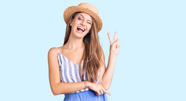 Genç, sarışın, yaz şapkası takan, gülümseyen, kameraya göz kırpan, parmaklarıyla zafer işareti yapan güzel bir kadın. İki numara.. 