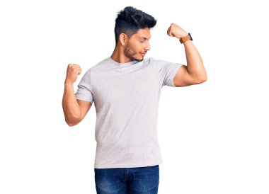 Yakışıklı, Latin Amerikalı, sıradan tişörtler giyen, gururla gülümseyen kol kaslarını gösteren genç adam. fitness konsepti. 