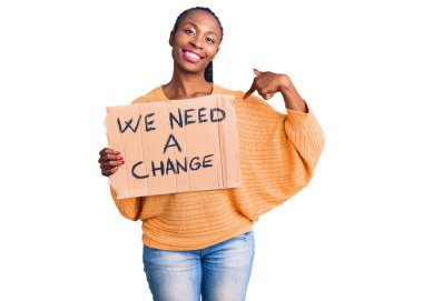 Genç Afro-Amerikan kadını elinde tutuyor Değişim pankartına ihtiyacımız var Mutlu ve gururlu gülümseyen birini işaret eden 