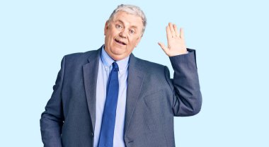 Kıdemli gri saçlı adam iş ceketi giyiyor. Merhaba diyor. Mutlu ve gülümseyen, dostça bir hoş geldin jesti. 