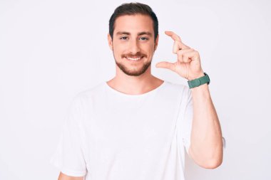 Genç, yakışıklı, günlük beyaz tişört giyen, gülümseyen, kendine güvenen, el hareketleriyle hareket eden, parmaklarıyla işaret eden ve kameraya bakan bir adam. ölçüm kavramı. 