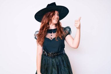 Cadı cadılar bayramı kostümü giyen genç ve güzel bir kadın gururlu görünüyor, gülümsüyor. Kenarda baş parmak hareketi yapıyor. 