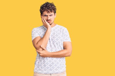 Kıvırcık saçlı, sıradan giyinen, yorgun görünen ve depresyondan sıkılmış kollarını kavuşturmuş genç yakışıklı bir adam.. 