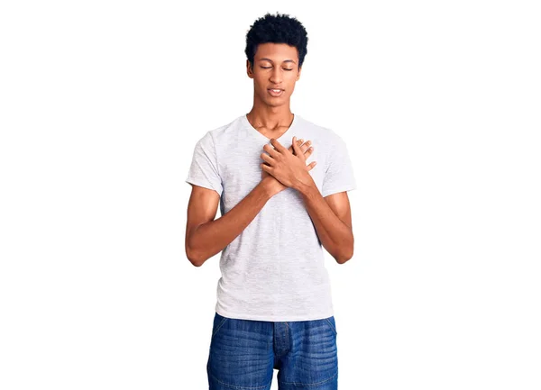 若いアフリカ系アメリカ人の男性は 目を閉じて胸に手で笑みを浮かべてカジュアルな白いTシャツを着て 顔に感謝のジェスチャー 健康の概念 — ストック写真