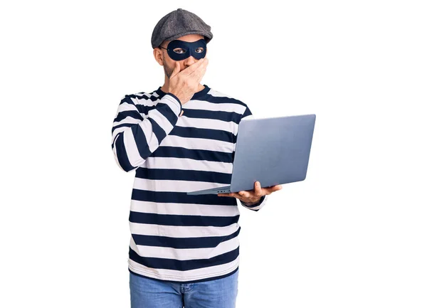 Young Handsome Man Wearing Burglar Mask Using Laptop Covering Mouth — Stock Photo, Image