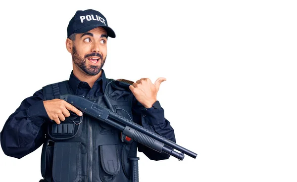 Joven Hispano Vistiendo Uniforme Policial Sosteniendo Escopeta Apuntando Con Pulgar —  Fotos de Stock