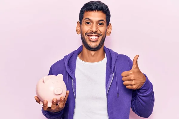 Jovem Latino Segurando Porquinho Banco Sorrindo Feliz Positivo Polegar Para — Fotografia de Stock