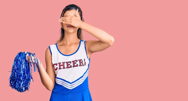 Young beautiful woman wearing cheerleader uniform smiling and laughing with hand on face covering eyes for surprise. blind concept.