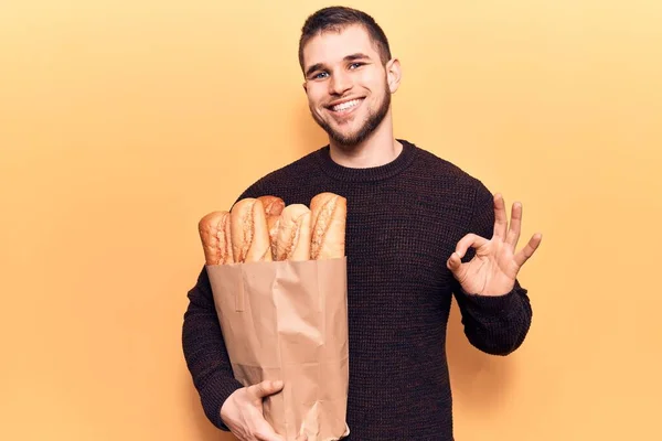 Joven Hombre Guapo Sosteniendo Bolsa Papel Con Pan Haciendo Signo —  Fotos de Stock