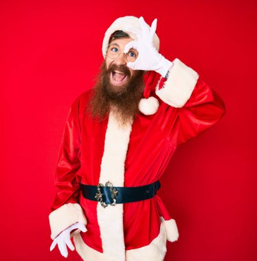 Yakışıklı, kızıl saçlı, uzun sakallı, Noel Baba kostümü giyen, gülümseyen, mutlu, el pençe divan duran, el pençe divan duran. 