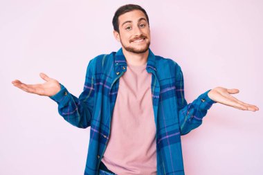 Gündelik kıyafetler giyen, gülümseyen, iki elini de açık tutan, sunan ve reklam karşılaştırması yapan genç yakışıklı bir adam. 