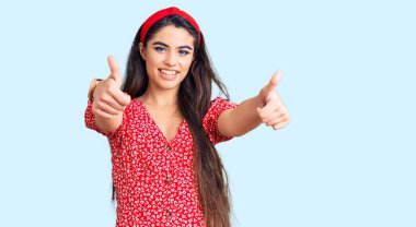 Yazlık elbiseler giyen esmer kız elleriyle olumlu jest yapıyor, gülümsüyor ve başarı için seviniyor. kazanan jest. 