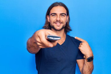 Uzaktan kumandayla uzaktan kumandayla gülümseyen mutlu ve gururlu birini işaret eden yakışıklı bir adam. 