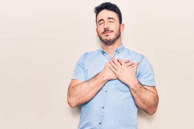 Gündelik kıyafetler giyen genç İspanyol adam elleri göğsünde gülümsüyor, gözleri kapalı ve yüzünde minnet ifadesi var. sağlık kavramı. 