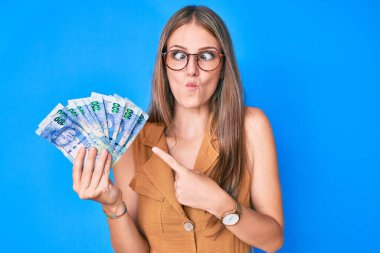 Güney Afrika rand banknotları tutan genç sarışın kız balık suratlı ve şaşı gözlü, çılgın ve komik.. 