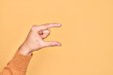 İzole edilmiş sarı arka plan üzerinde parmaklarını gösteren beyaz bir adamın eli. Görünmez bir şeyi alıp, parmaklarıyla uzayı gösteren bir nesneyi tutuyor.