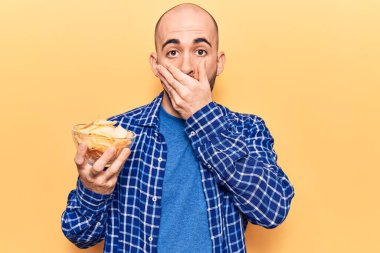 Genç yakışıklı kel adam elinde patates cipsi, ağzı ağızla kaplanmış, şok olmuş ve hata yapmaktan korkan. şaşırmış ifade 