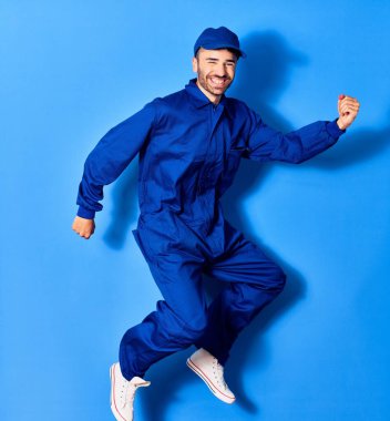 Genç yakışıklı İspanyol ressam üniforması ve şapkalı mutlu gülümsüyor. Yüzünde gülücükle zıpla kazanan imzayı izole edilmiş mavi arka planda yumruklarla at.