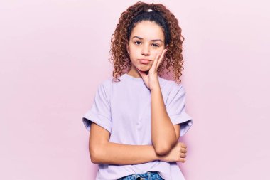 Kıvırcık saçlı, günlük kıyafetler giyen, yorgun görünen ve depresyondan sıkılmış kollarını kavuşturan güzel bir kız çocuğu.. 