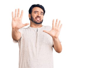 Günlük giysiler giyen genç İspanyol adam korku ifadesinden korkuyor ve dehşete düşüyor. El hareketlerini durdur, şok içinde bağır. panik konsepti. 