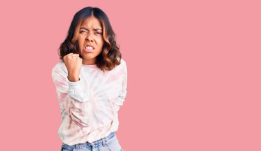 Genç, güzel, karışık ırklı, günlük kravat boyası eşofmanı giyen kızgın, kızgın ve kızgın bir şekilde yumruğunu kaldıran öfkeli bir kadın. öfke ve agresif konsept. 